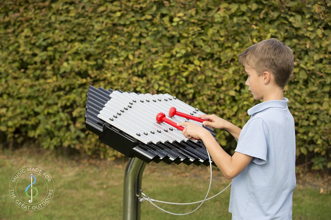 schoolboy in park playing outdoor musical xylophone with silver notes and black resonators
