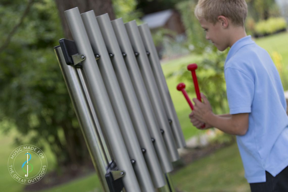 schoolboy playing mounted musical chimes in park