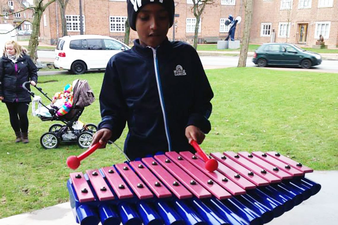 young boy playing a blue and pink xylophone in a playground