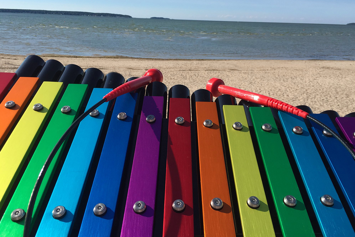 rainbow colored musical notes on an outdoor xylophone with a beach in the background