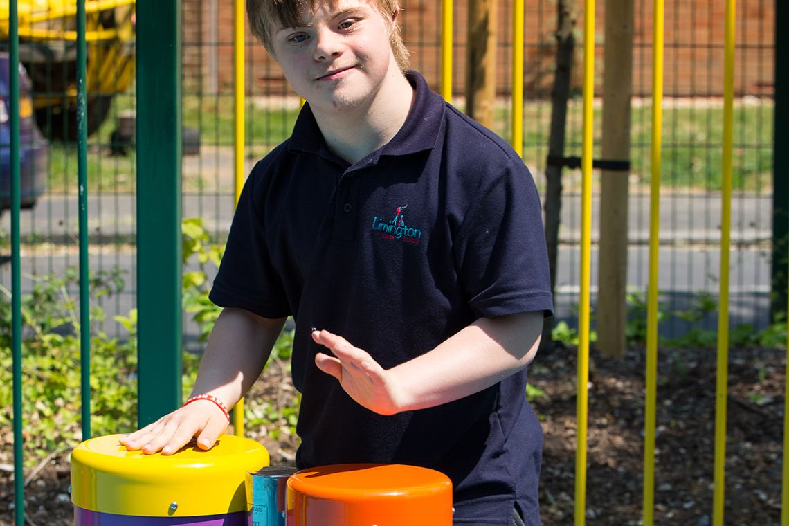 boy with special needs playing colourful outdoor drums in a school playground