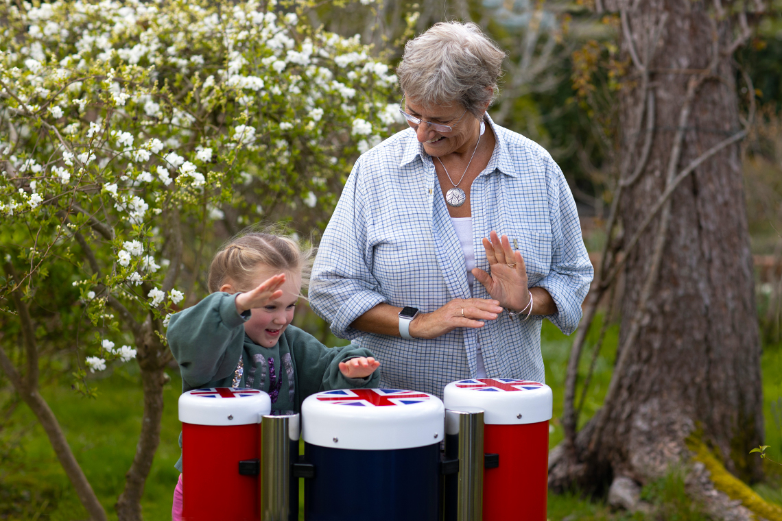 an older female adult and young girl playing outdoor conga drums in red white and blue with union flag tops