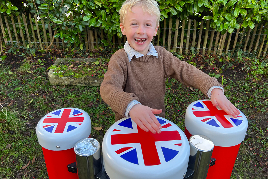 a young blond boy playing red white and blue outdoor conga drums