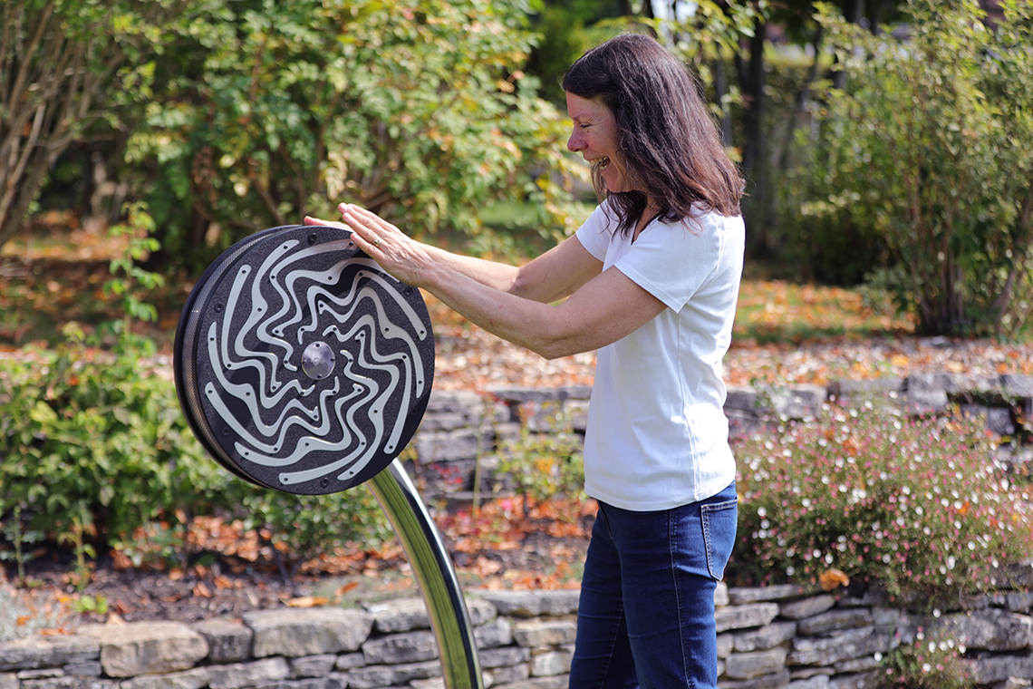 a lady playing with a black and silver spinning rain wheel in a garden