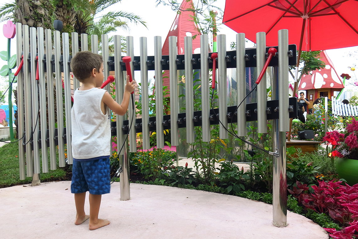 a small barefoot little boy playing a set of large musical chimes in a music park or playground