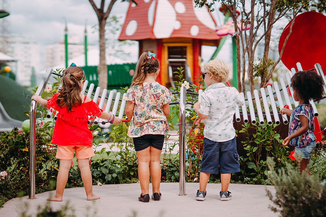 the backs of four young children all playing a large outdoor musical instrument in a music park or playgound