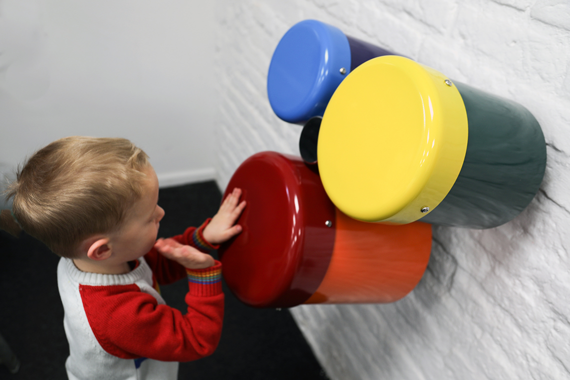 A group of three different sized wall mounted rainbow coloured outdoor bongo drums designed for smaller children