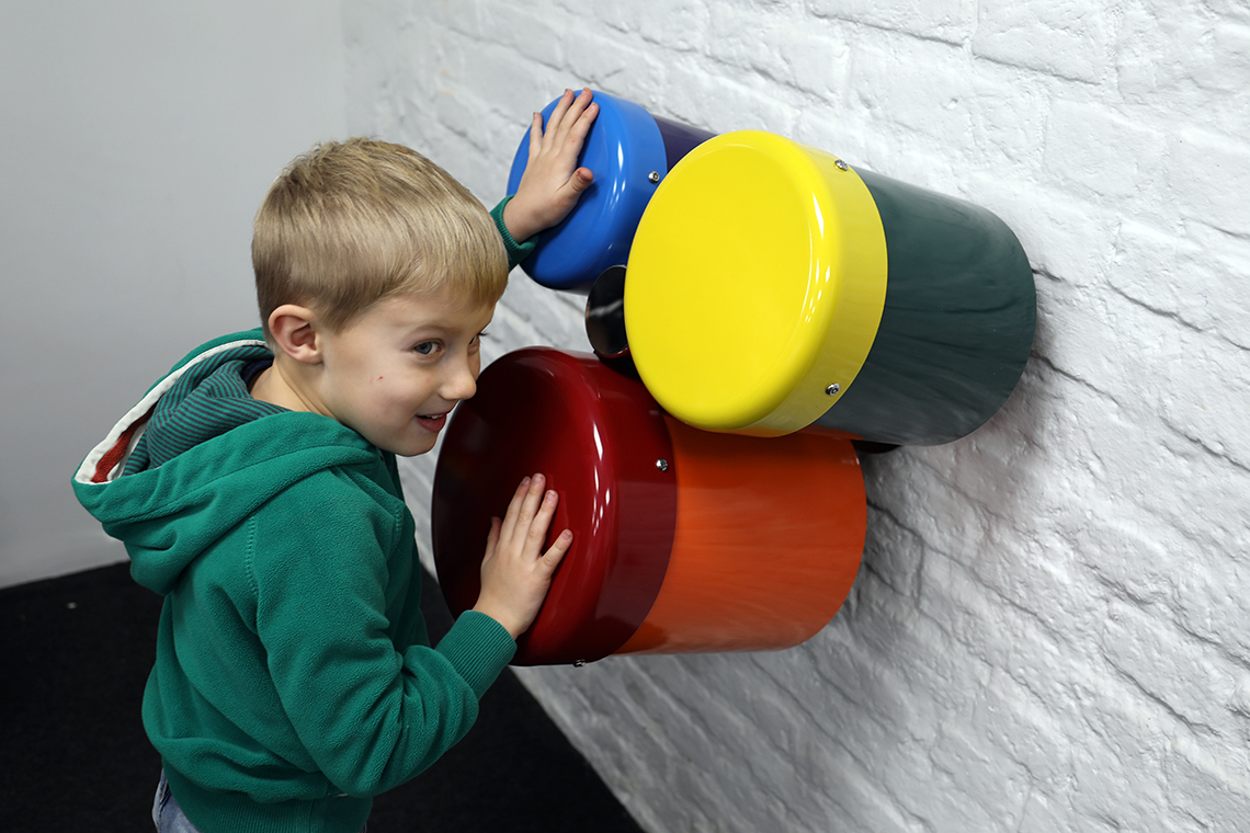 A group of three different sized wall mounted rainbow coloured outdoor bongo drums designed for smaller children