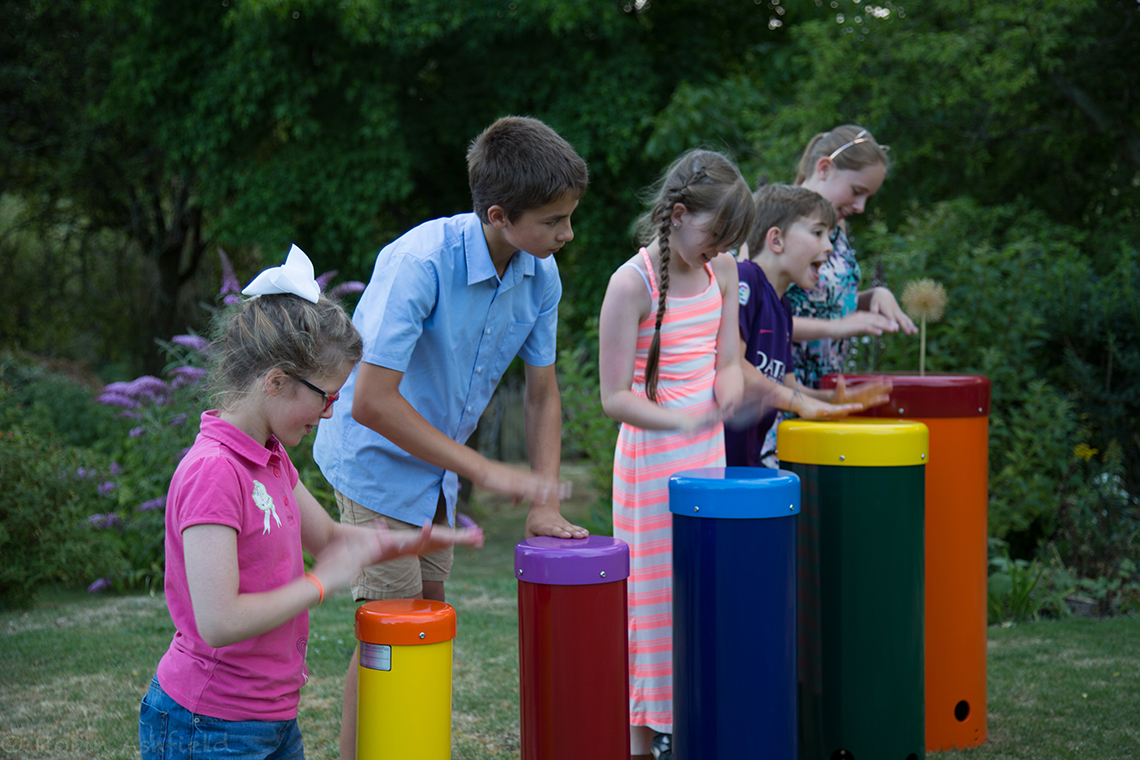 five children playing on a rainbow coloured set of samba drums in the outdoors