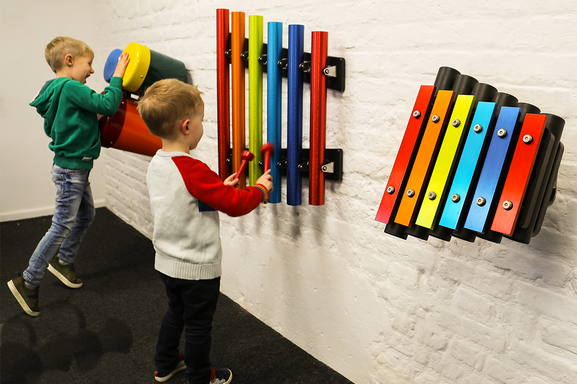 A collection of small outdoor musical instruments mounted on the wall suitable for nursery or kindergarten aged children