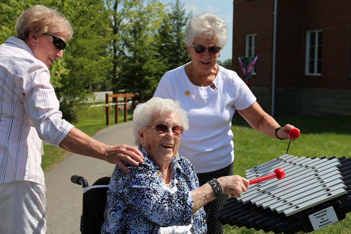 older lady in a wheelchair laughing and playing a xylophone outdoors
