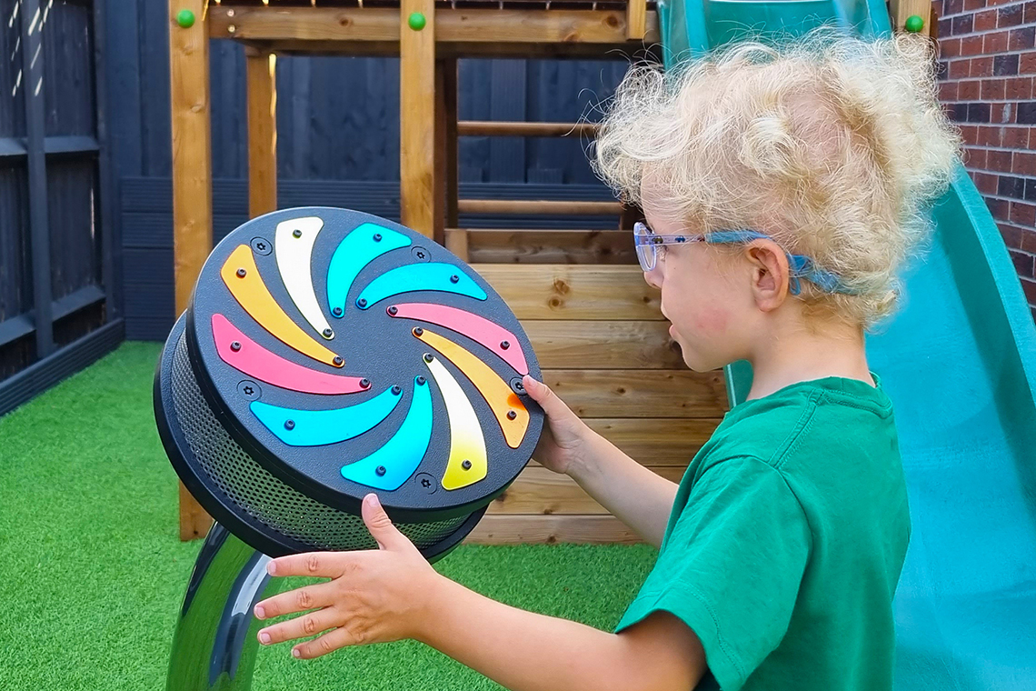 a young blond boy with special needs playing a small outdoor rain wheel with rainbow colored flashes on the front