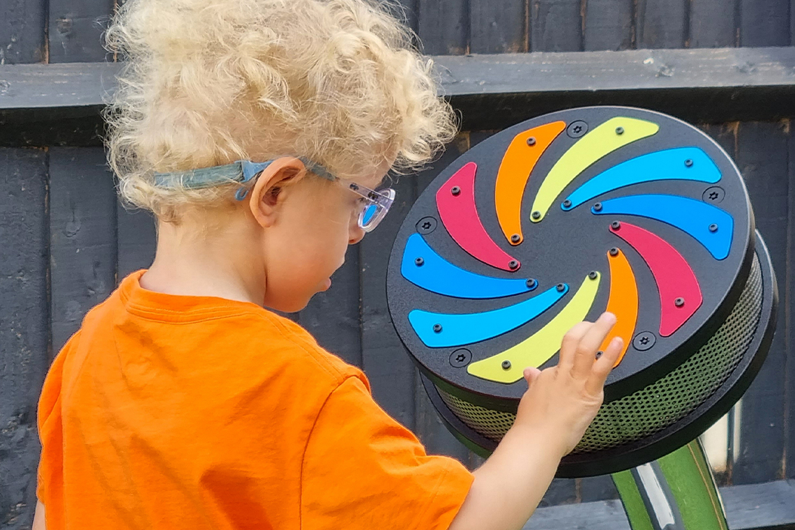 a young boy with special needs wearing an orange t shirt and playing an outdoor rain wheel in the playground 