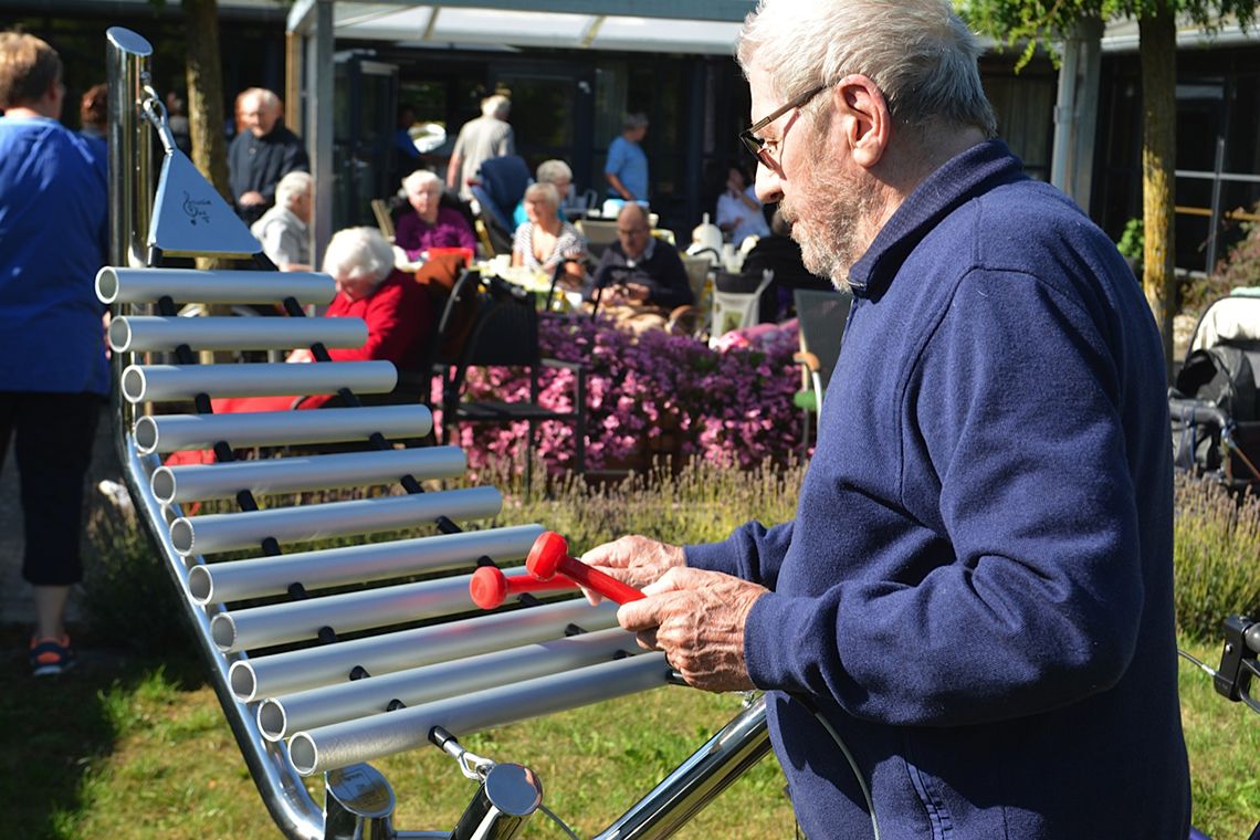 Older man playing an outdoor xylophone in care ome garden