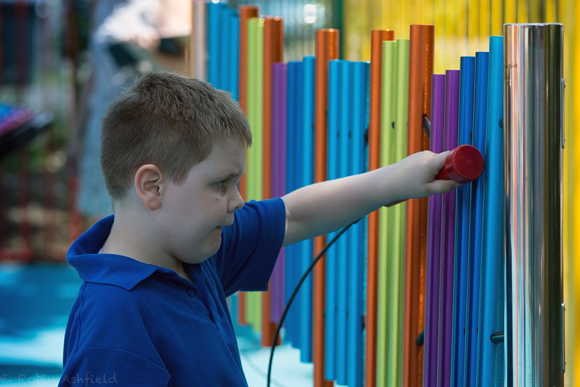 boys with special needs playing rainbow coloured chimes outdoors